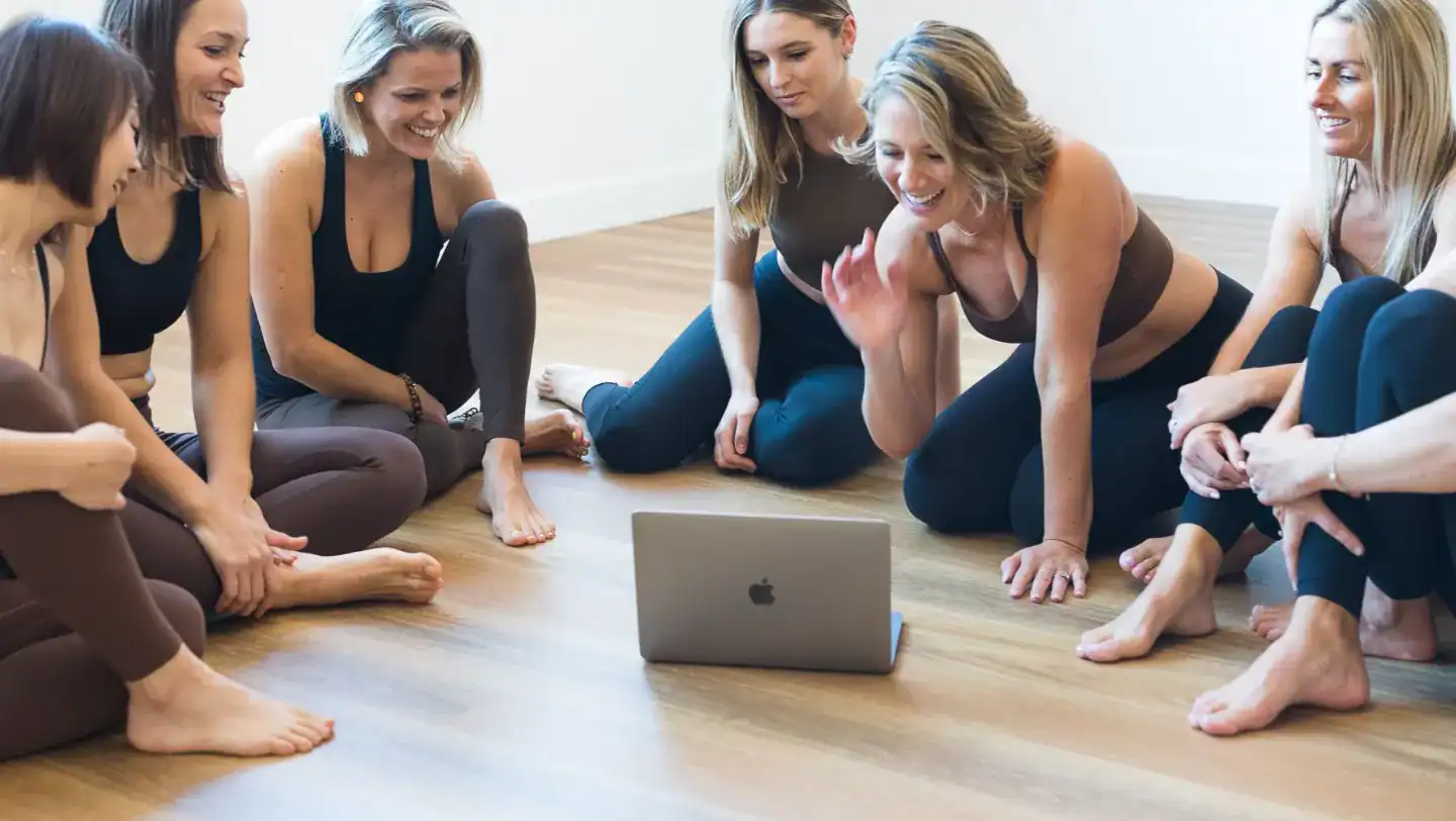 Group of Village Pilates clients gathered around a laptop, smiling